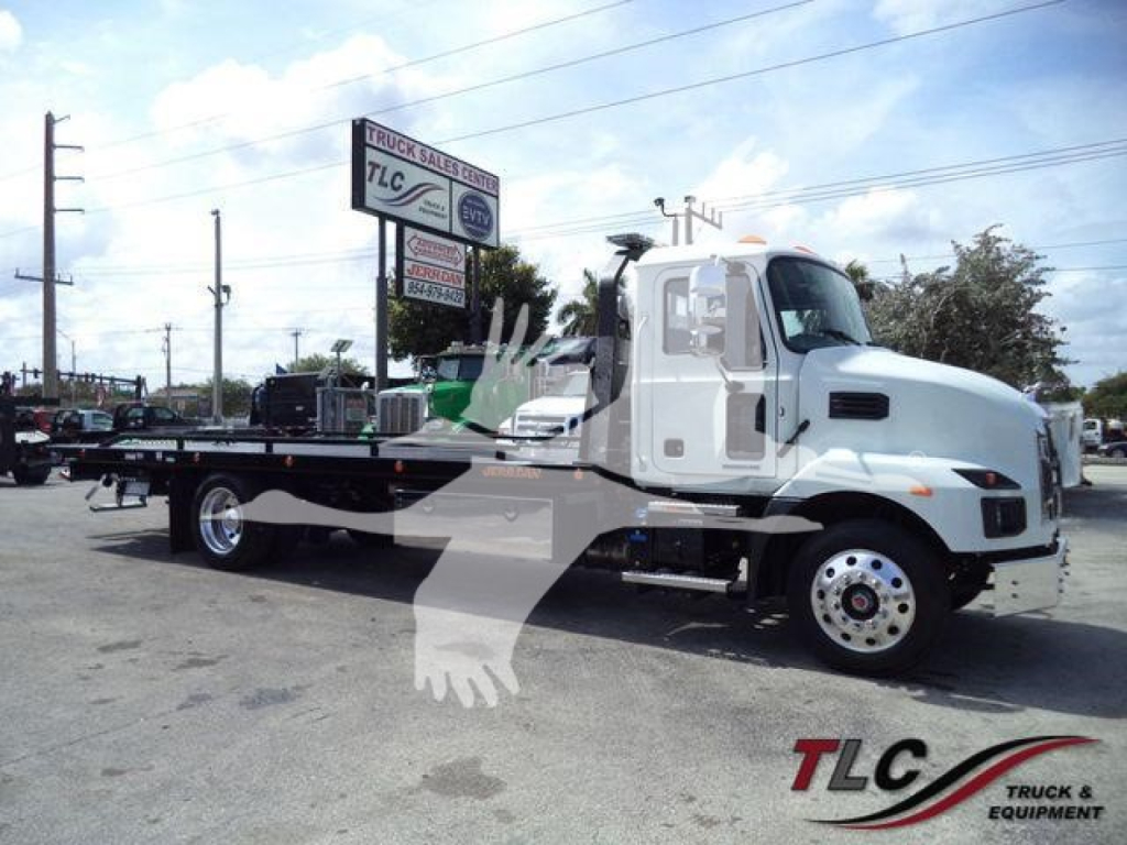 Flatbed tow truck showing new 2027 Mack MD6 with rollback equipment and dealer lot in background.