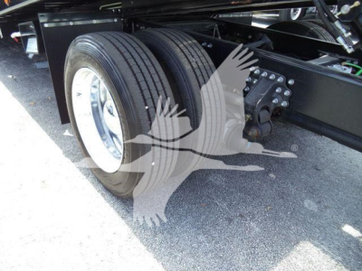Dual rear axle with tire pair and suspension brackets under Mack MD6 rollback truck showing wheel, hub, and leaf-spring mount.