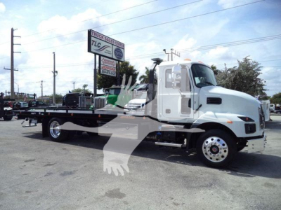 MD6 roll-back truck from a side view with flatbed; Mack emblem on hood; sign in background; stock number J13303; white cab with black flatbed.