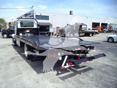 MD6 Mack rollback truck flatbed in a dealership lot, rear view showing loading ramps and deck with reflective lights