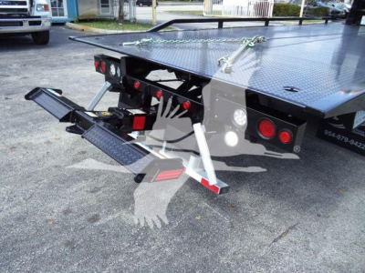 Panel-mount platform truck with fold-down rear step and safety chain on a flatbed rollback trailer showing rear bumper lights and hydraulic support leg.