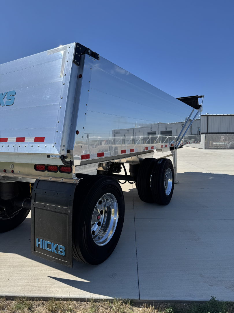 Hicks FL2827 spread axle dump trailer side view showing aluminum dump body, dual rear axles, mudflaps with HICKS branding, and reflective tape.