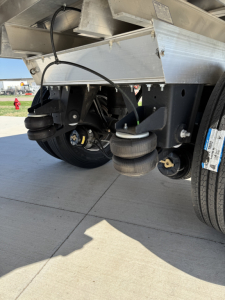 Trailer undercarriage showing spread axle suspension with air and coil components, metal frame, and wheels.