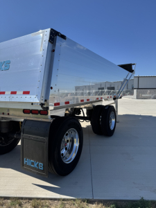 Hicks FL2827 spread axle dump trailer side view showing aluminum dump body, dual rear axles, mudflaps with HICKS branding, and reflective tape.