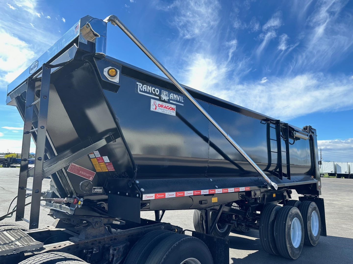 Ranco quarter frame steel end dump trailer showing Triple-axle configuration and rear tailgate with safety chains and reflective decals.
