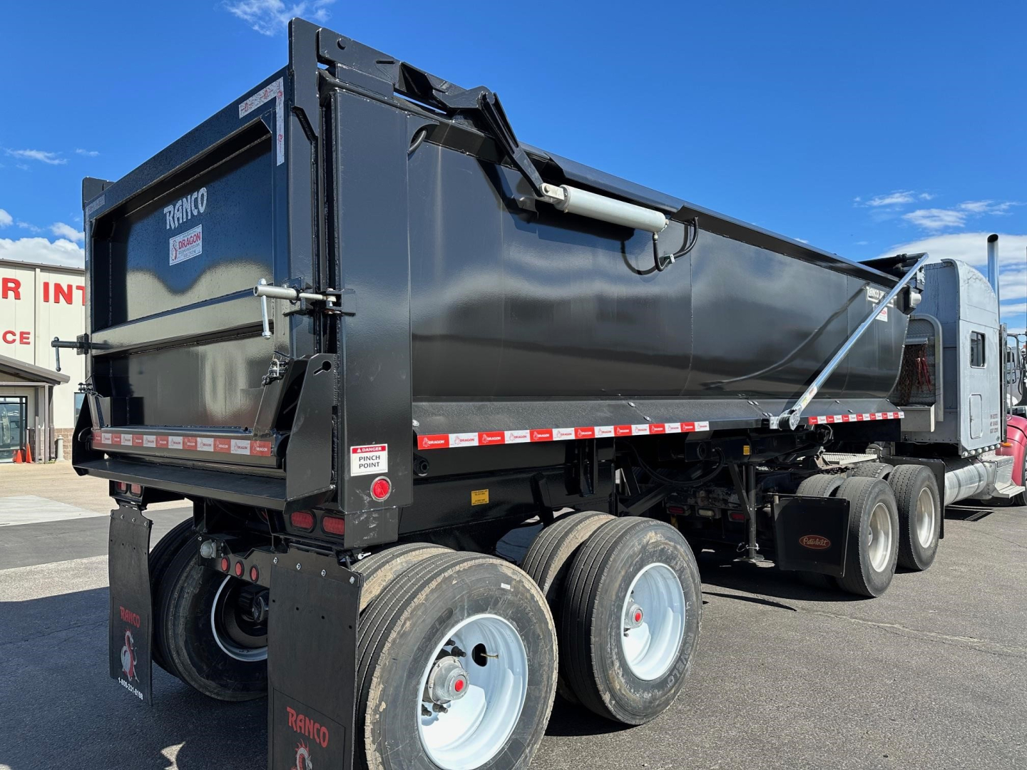 Ranco quarter frame steel end dump trailer with three axles, black finish, side markings, and hydraulic used in hauling aggregate.
