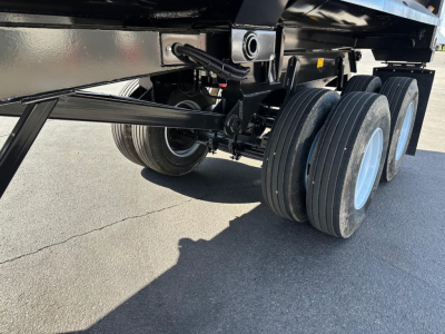 Trailer axle area showing triple-axle configuration with black frame and light blue wheels. Visible are suspension components and supports under a steel end dump trailer.