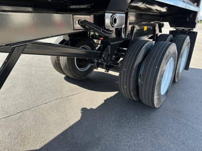 Trailer underside showing tandem axle wheels and suspension of a steel end dump trailer.