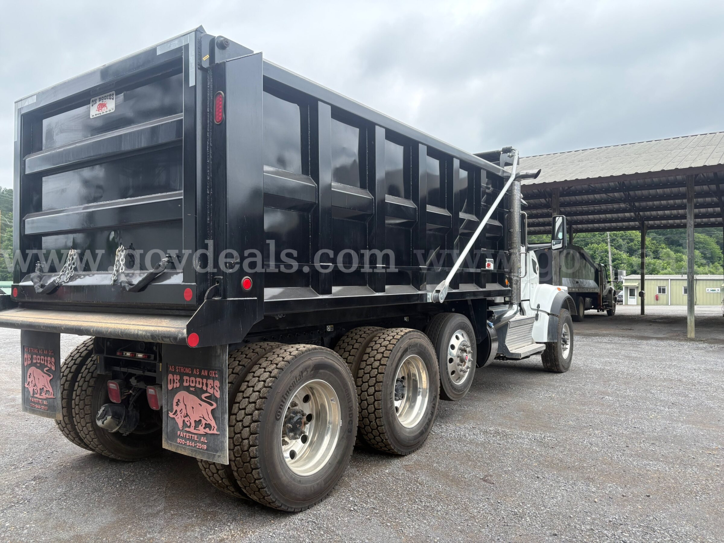 Peterbilt 377 dump truck rear and side view showing heavy-duty dump bed and dual rear axles with large tires; black paint; stock number and trim visible.