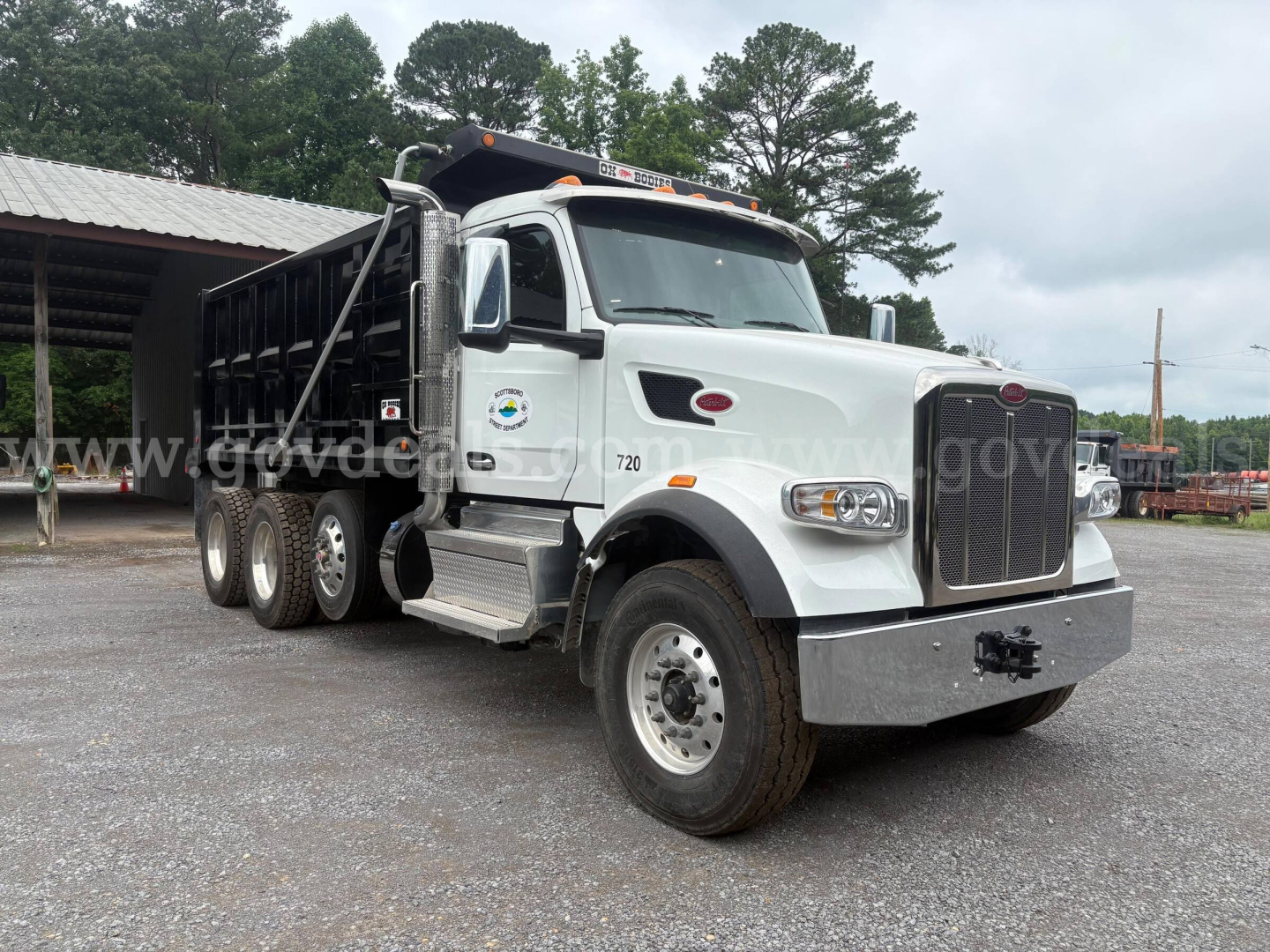 Peterbilt 377 dump truck in white, front-right view with black dump bed, heavy-duty bumper, multiple rear axles, and Peterbilt emblem on grille.