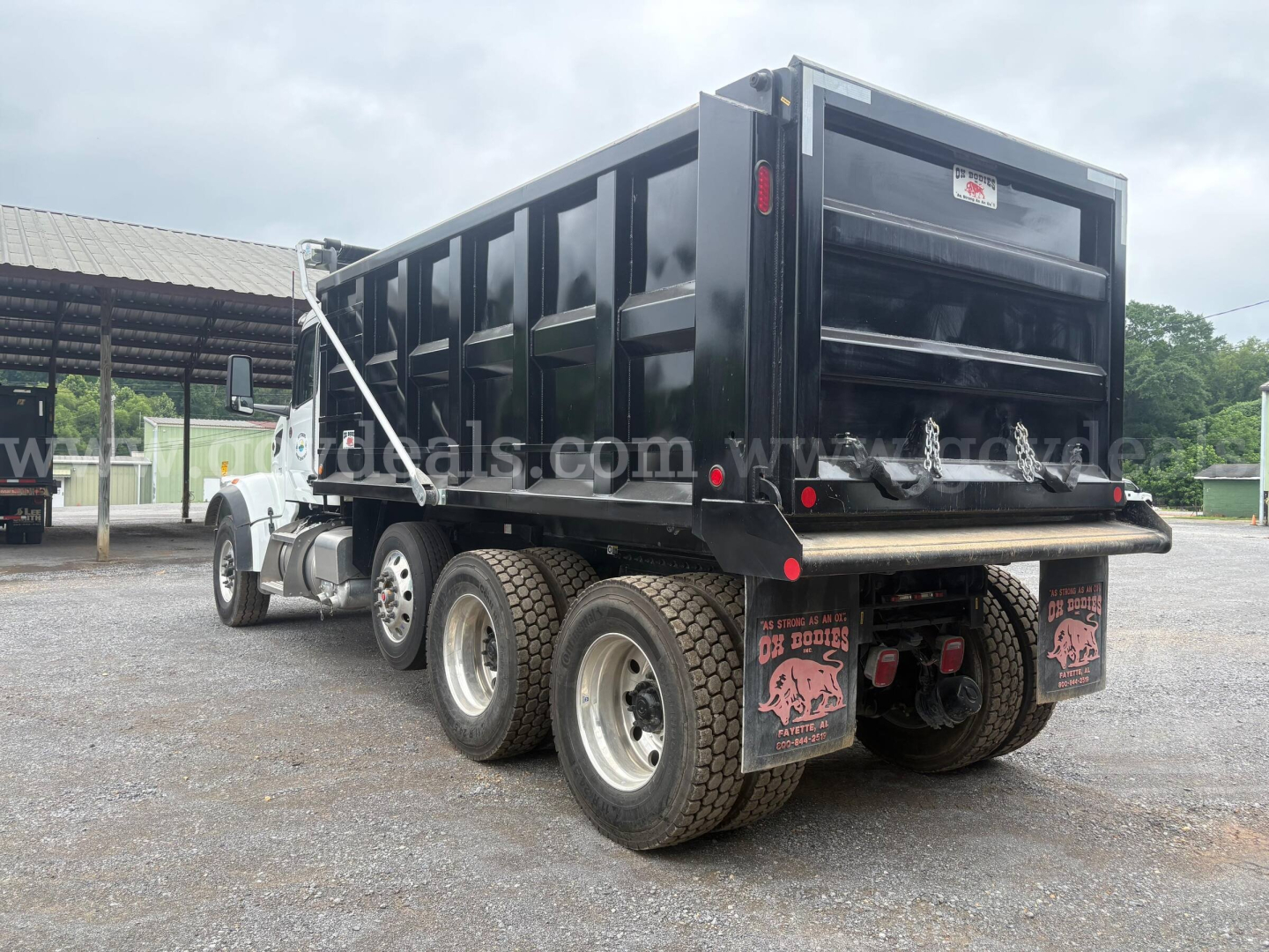 Peterbilt 377 dump truck rear-left view showing dump bed, dual rear axles, mud flaps, and rear bumper with taillights.