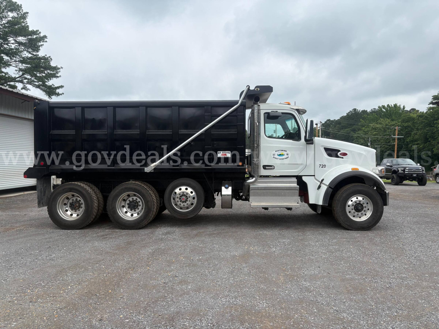 Peterbilt 377 dump truck side view showing black dump bed, white cab, six wheels, and hydraulic bed lifting arm.
