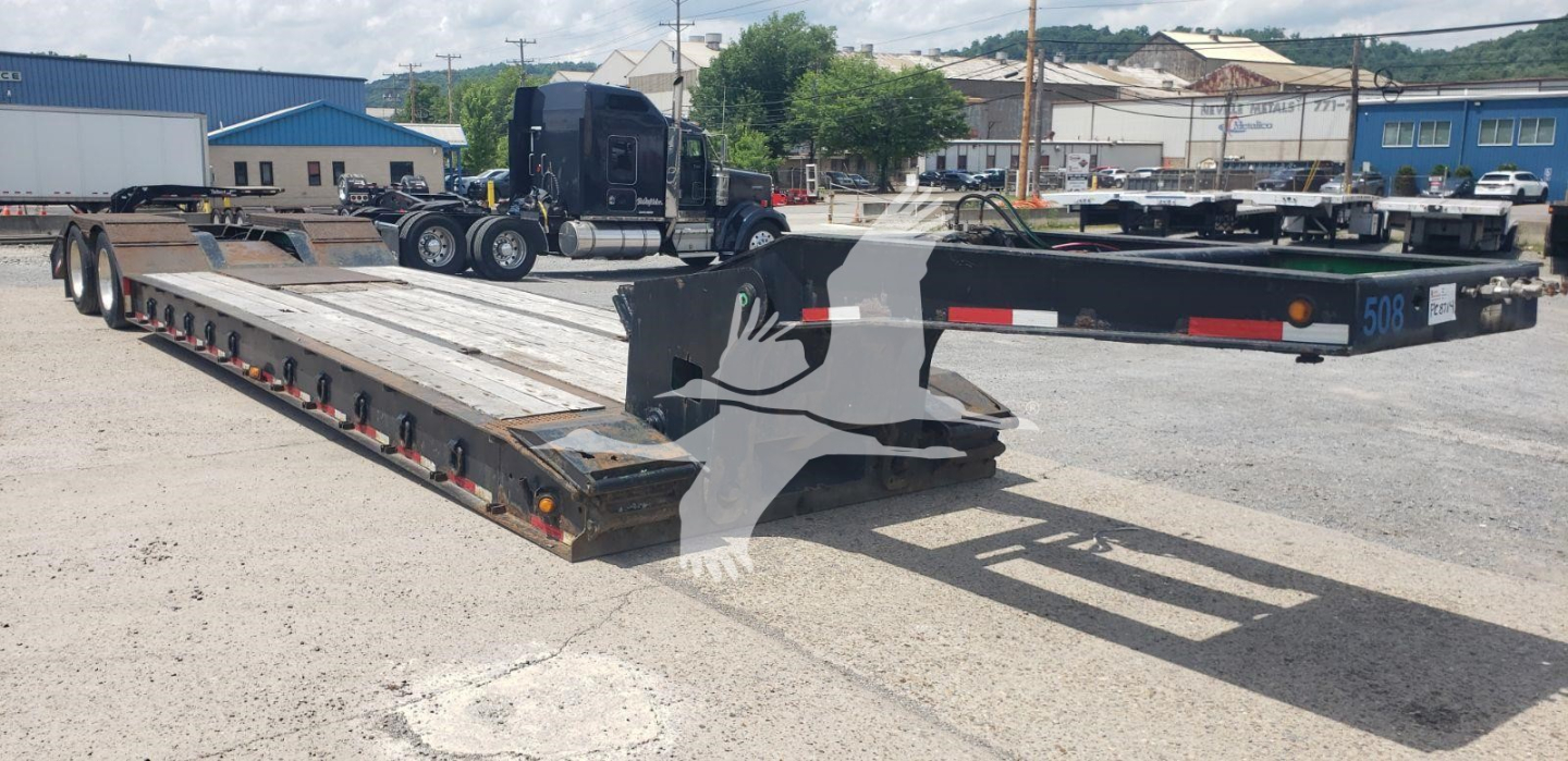 Lowboy trailer with extendable beavertail showing long steel deck and access ramps, Load King branding, and fittings along sides.