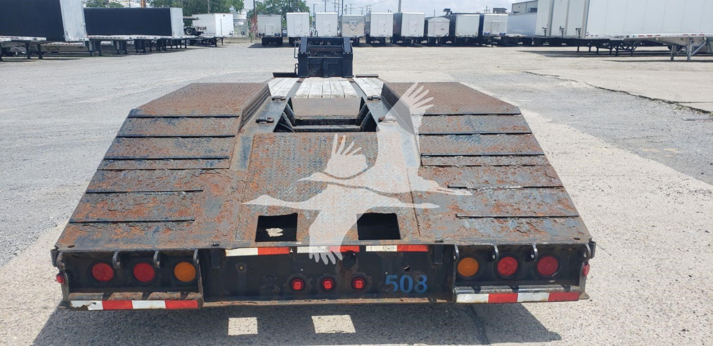 Flatbed trailer rear view showing beavertail deck with rusted surface and taillights, Load King branding not visible.
