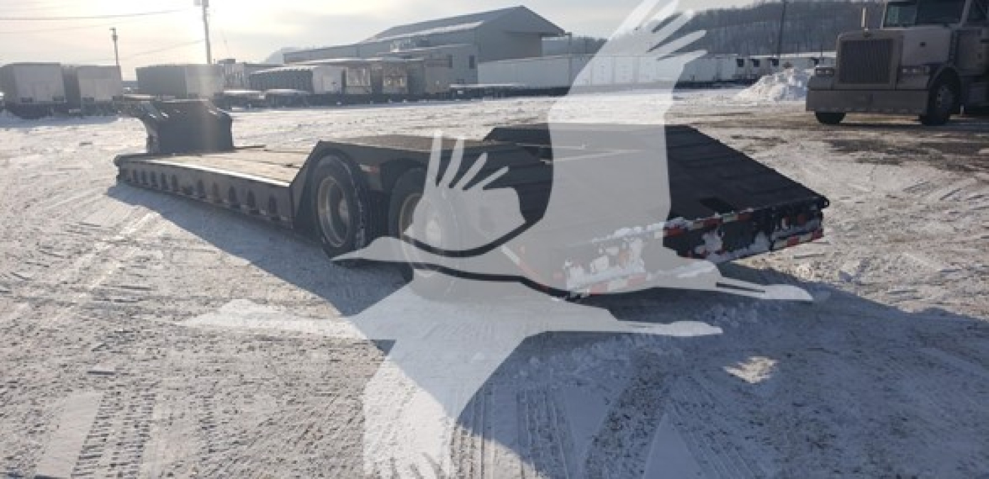 Lowboy trailer showing Load King beavertail design with long flatbed and rear ramps, snow-covered ground.