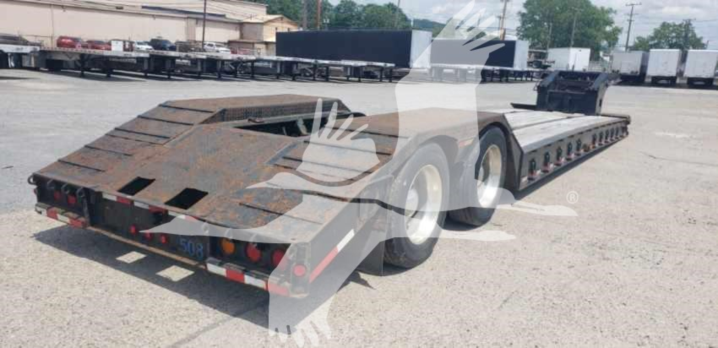 Load King lowboy trailer shown from rear-left side; long, multi-axle beavertail with ramp and rust-free steel surface; taillights visible.