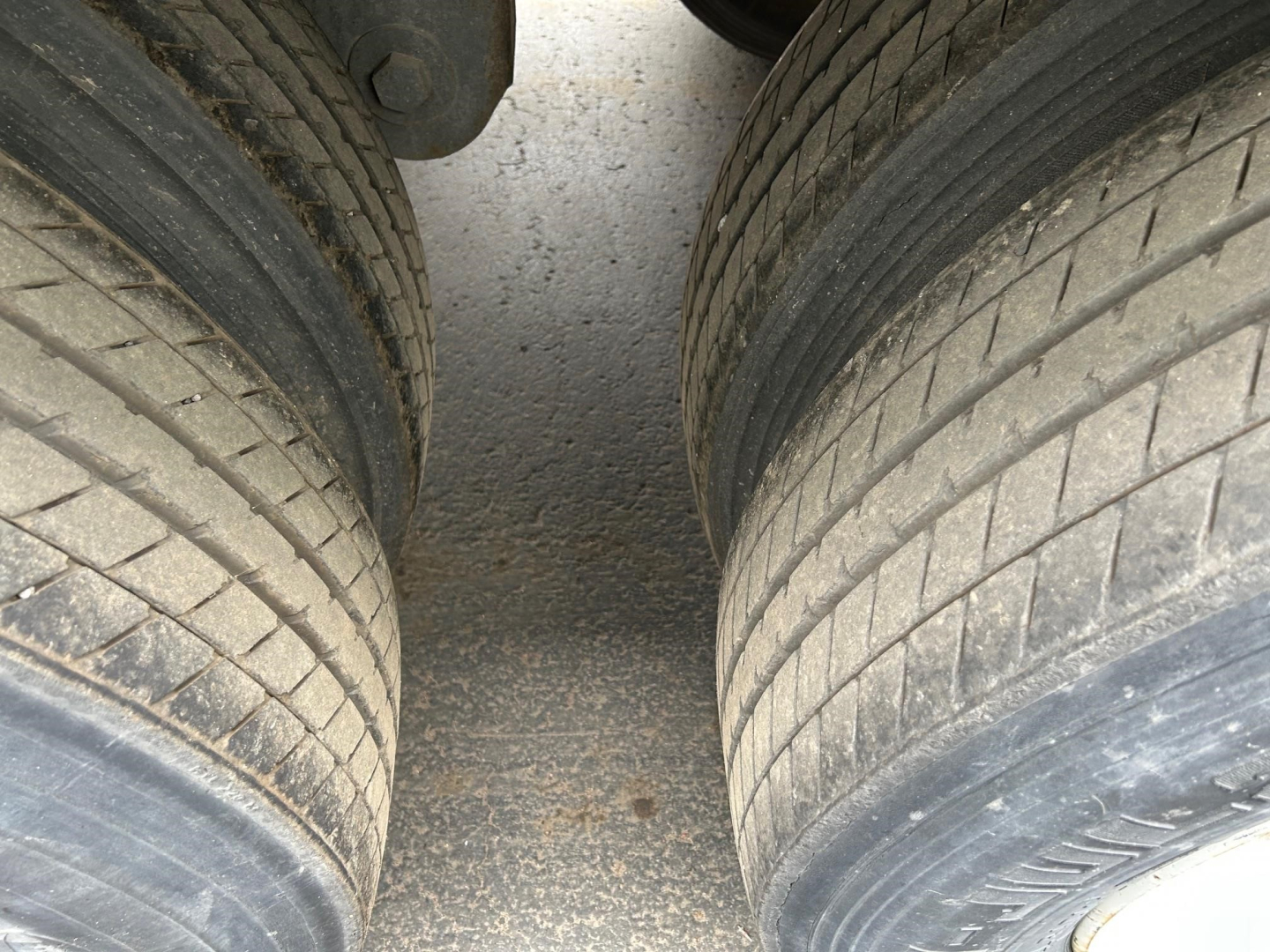 Trailer wheelview showing dual rear axles with tires and road grime on the surface.
