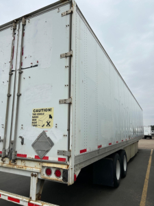 Trailer rear-left view of a Stoughton air ride dry van trailer showing cargo doors, caution label, and rear lights.