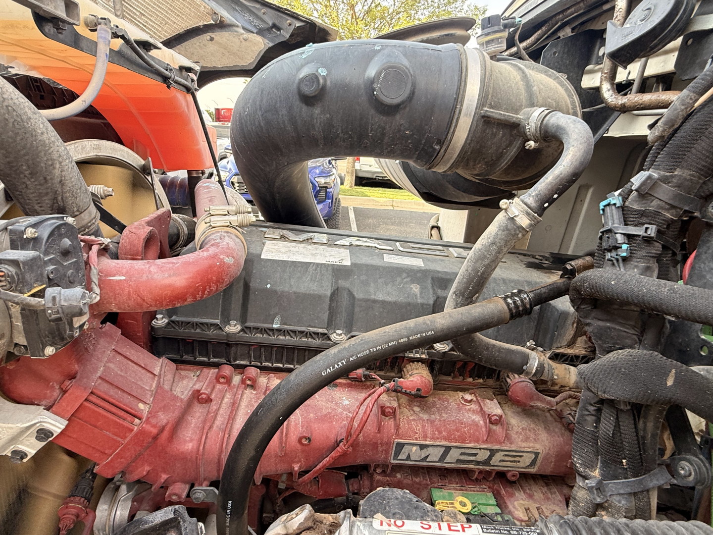 Mack Pinnacle engine bay showing MBE diesel engine with red intake manifold, black turbocharger piping, and various hoses and cables visible.