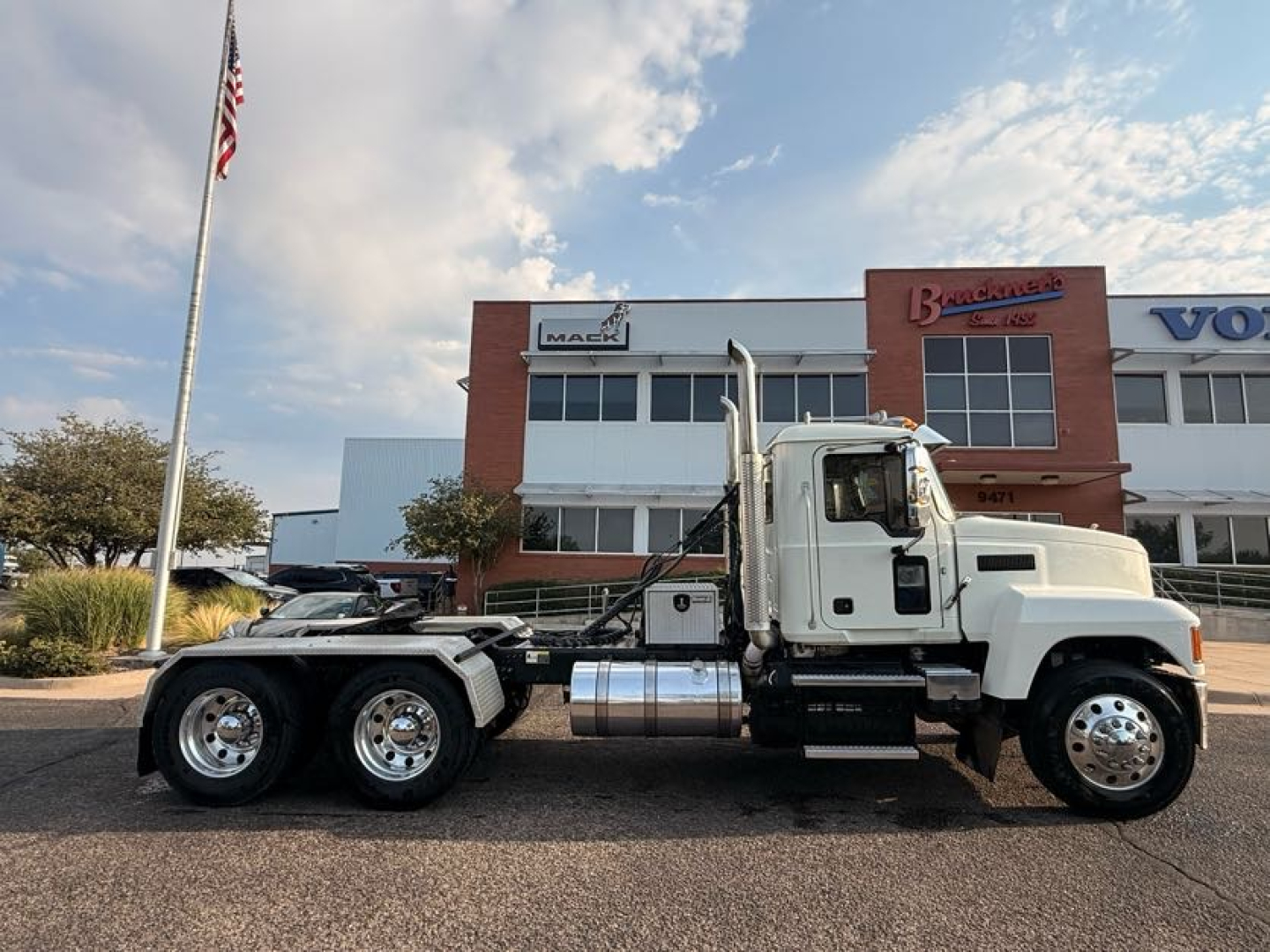 Side view of a white 2020 Mack Pinnacle conventional daycab truck showing dual rear axles with chrome fuel tanks and steps.