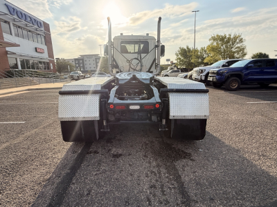 Conventional daycab truck from rear showing hitch and dual fuel/utility step compartments under the cab, with parking lot and dealership building in background.