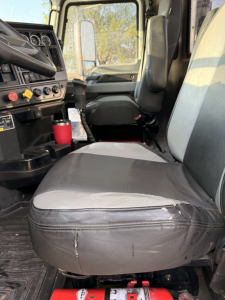 Front cab interior of a 2020 Mack Pinnacle daycab showing driver seat and passenger seat, steering wheel visible, dashboard controls, floor mats, and gear lever.