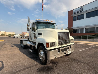 Mack Pinnacle day cab truck in a lot with front grille, chrome bumper, dual exhaust stacks, and large headlights. Visible text on building reads Mack. VIN tag not legible.