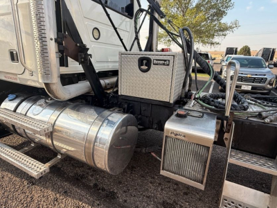 Mack Pinnacle truck cab area showing a chrome cylindrical fuel tank, aluminum toolbox, Hydramatic or Hydrive system with fuel lines and steps; metallic panels and hoses visible.