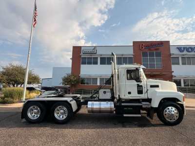 Side view of a white 2020 Mack Pinnacle conventional daycab truck showing dual rear axles with chrome fuel tanks and steps.