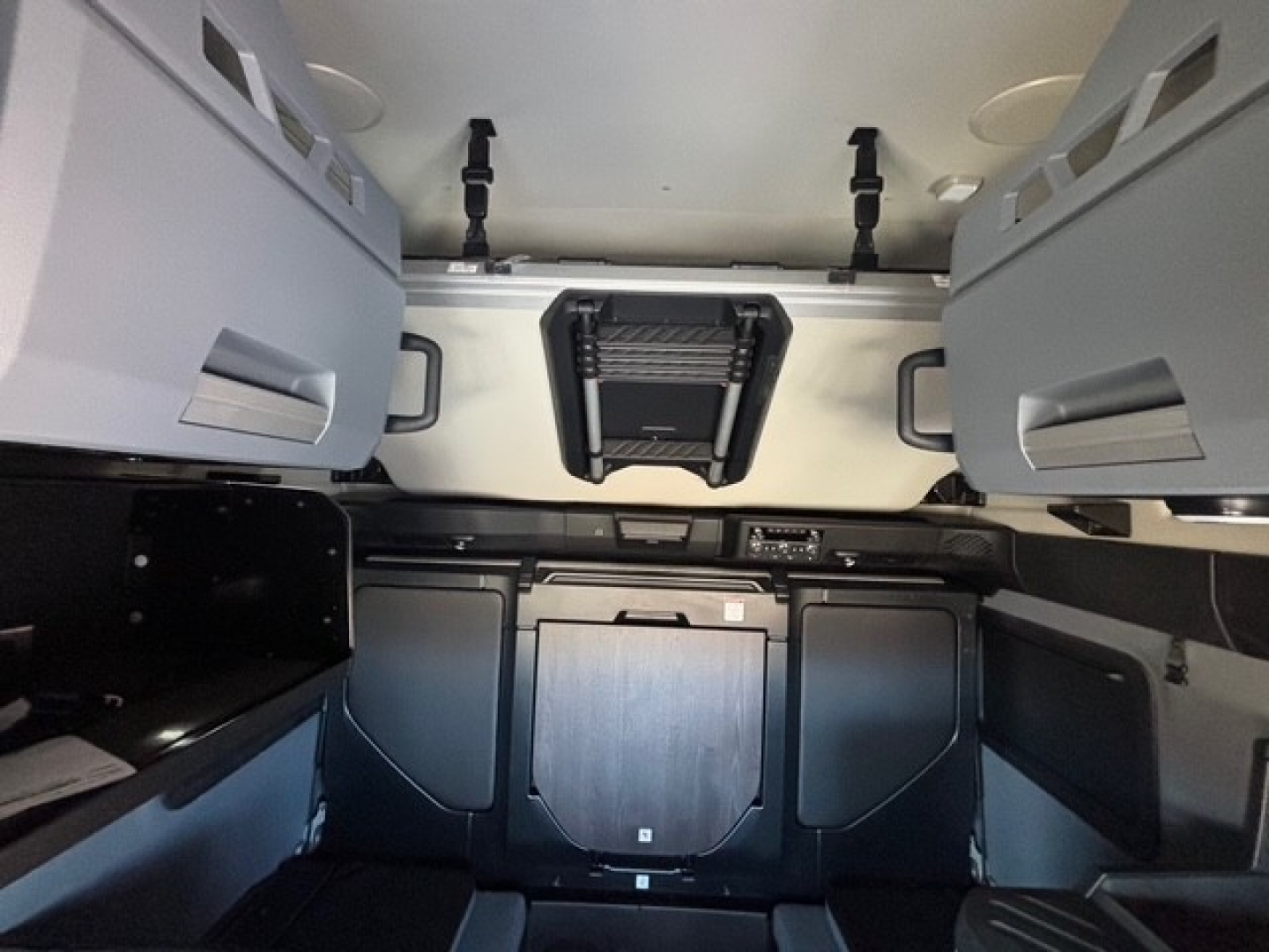 Cab/driver area of a new Mack PR64T76H sleeper tractor showing dashboard, overhead storage, and central console with various panels.