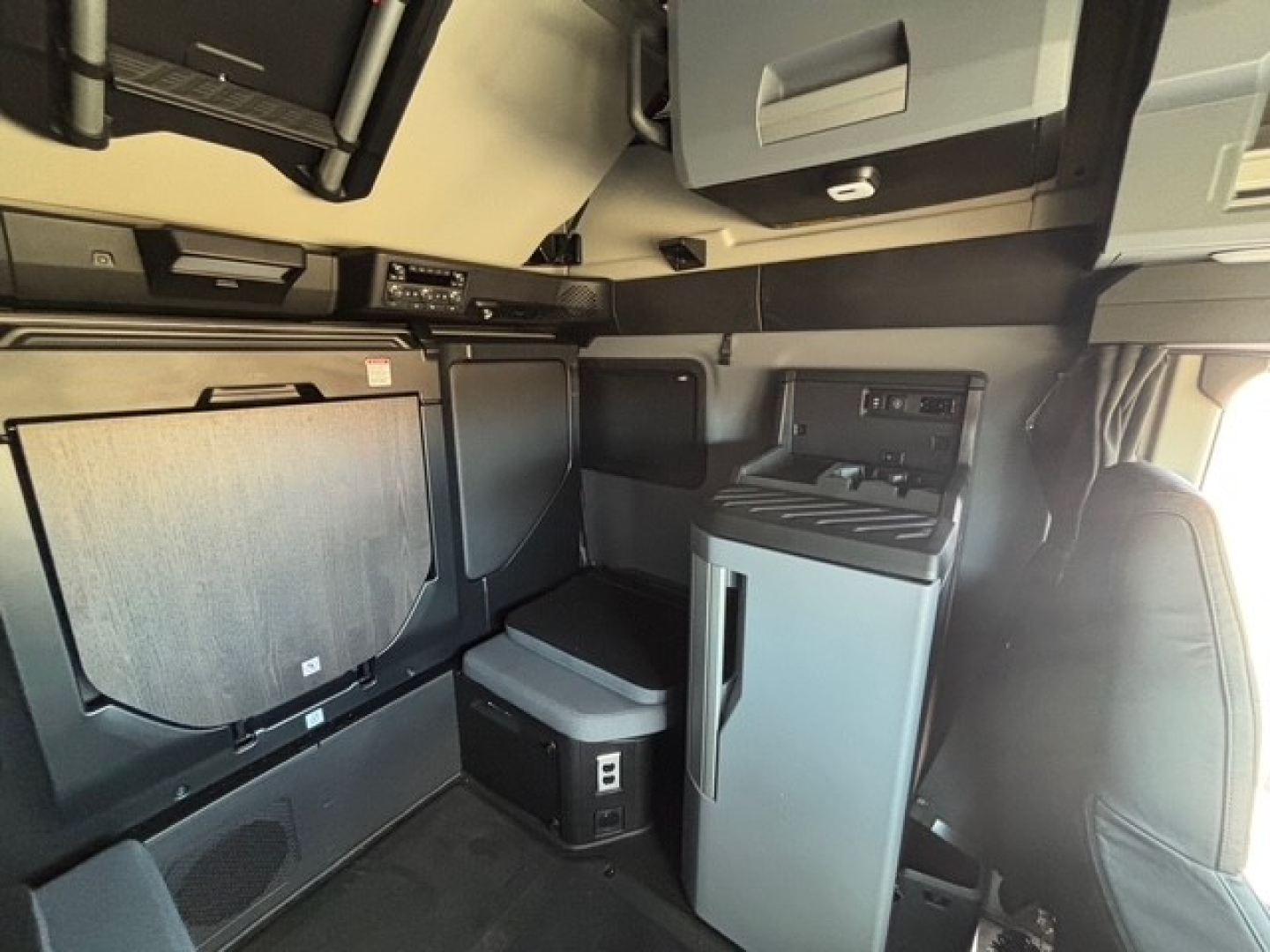 Cabin interior of a new Mack PR64T76H truck showing storage cabinet, refrigerator, and overhead compartments.