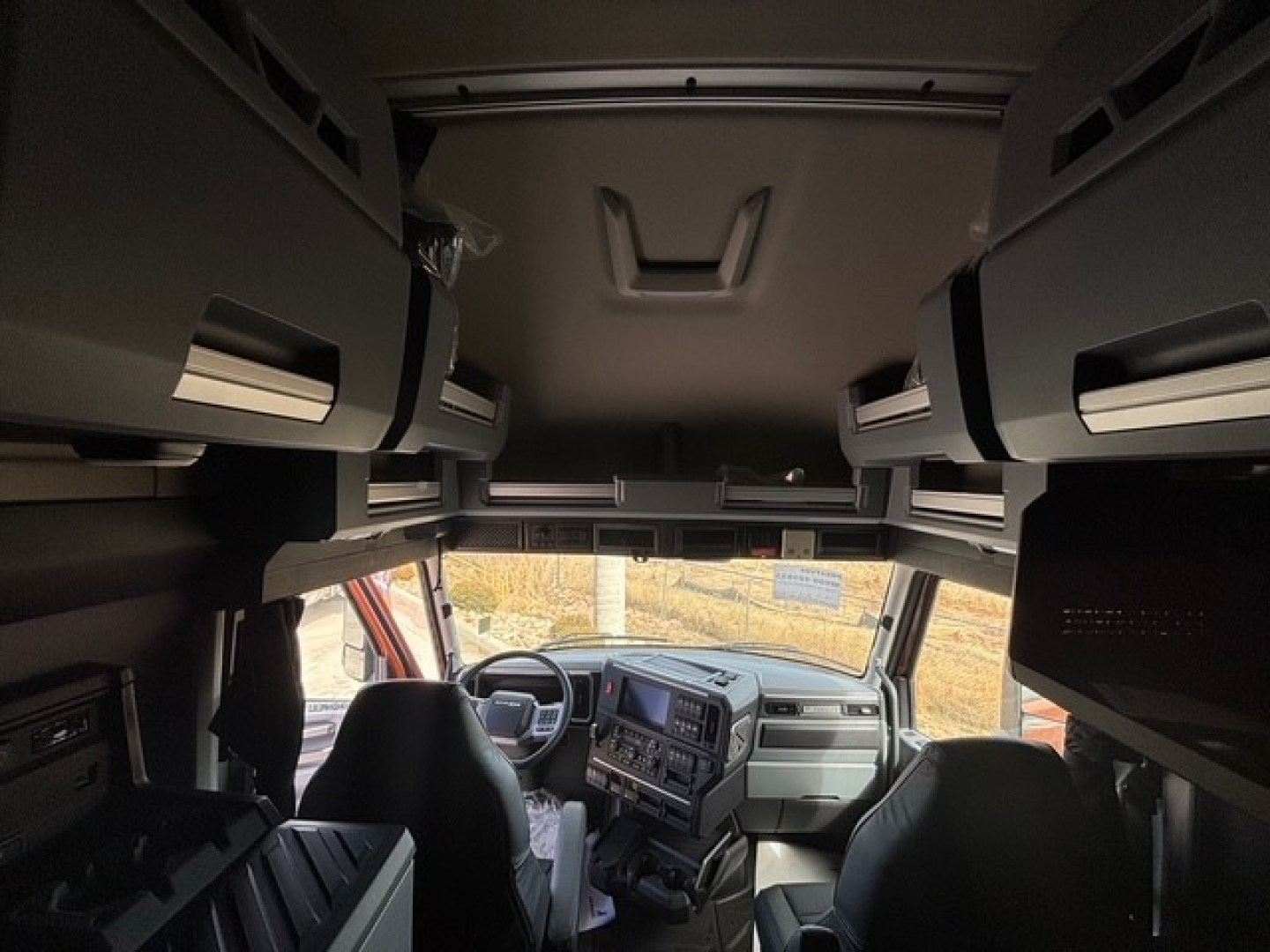 Cabin interior of a Mack PR64T76H truck showing overhead bunk storage compartments and dashboard with steering wheel