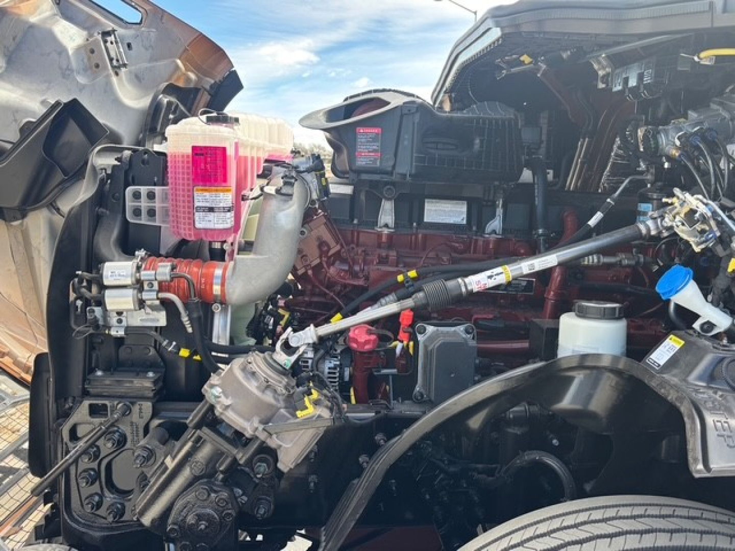 Mack PR64T76H engine bay showing pink coolant reservoir, turbocharger, hoses, wiring harnesses, and engine components.