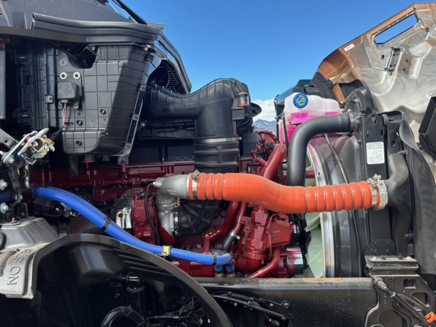 Truck engine bay showing blue and orange hoses connected to engine, radiator, and surrounding components.