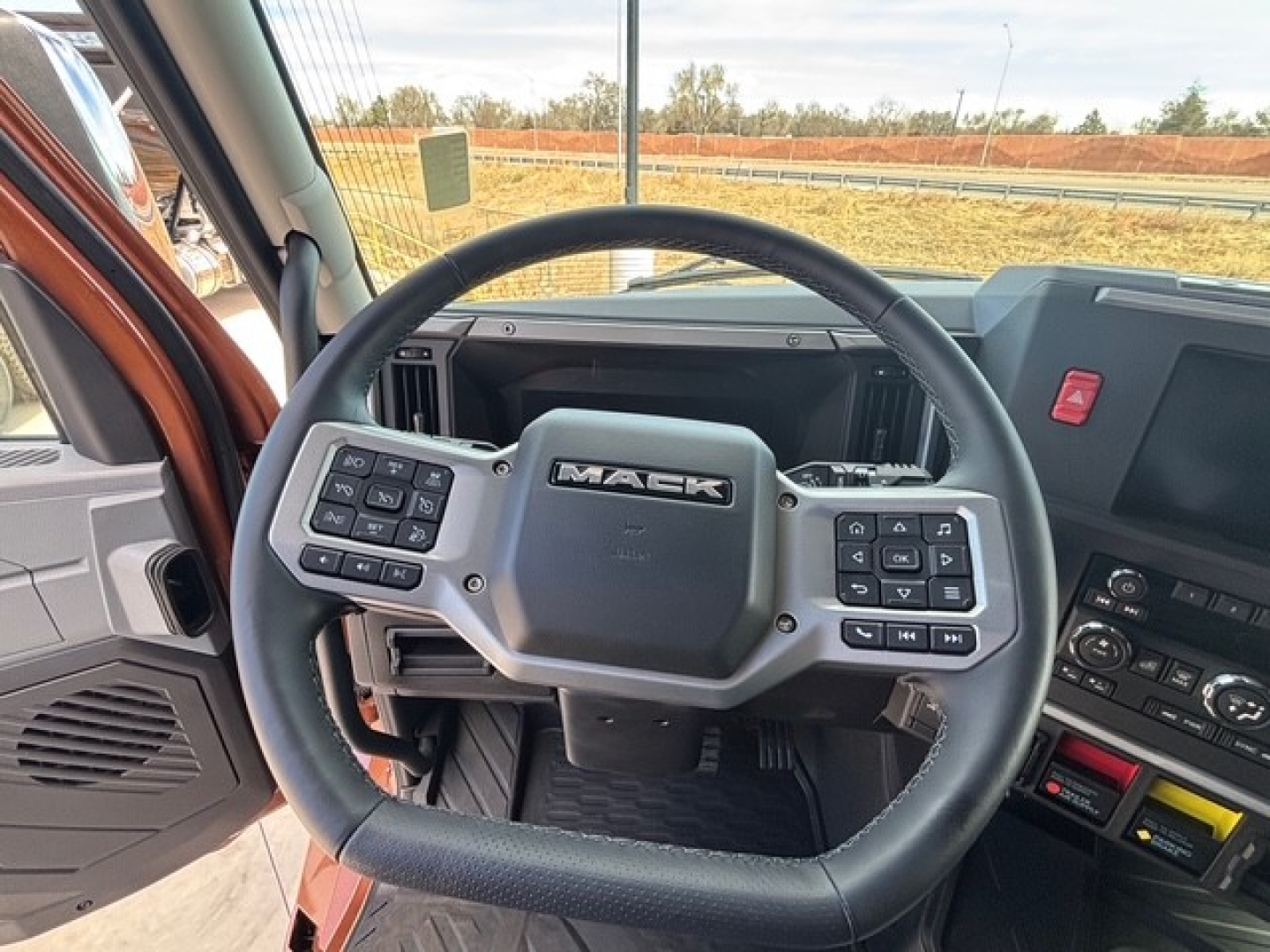 Mack PR64T76H truck interior showing steering wheel with Mack logo and control buttons, dashboard and center console visible.