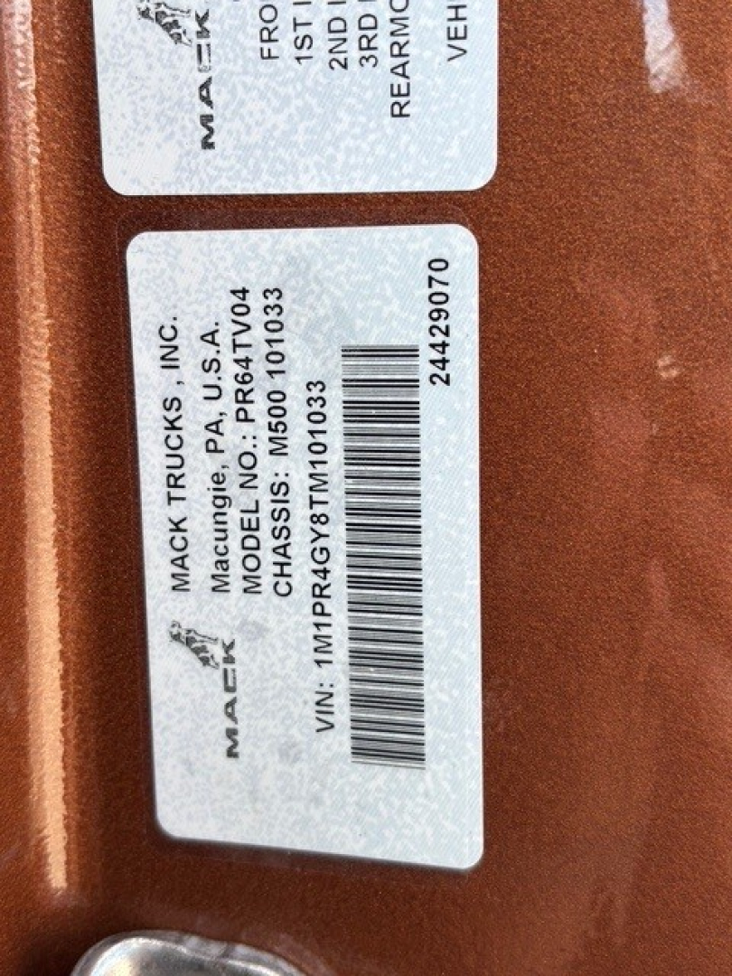 Mack Trucks label on door jamb showing VIN 1M1PR4GY8TM101033 and model/stock details, with barcode and various white stickers.