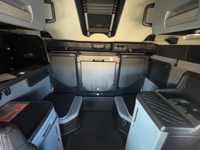 Cab interior of a new Mack PR64T76H sleeper with bunk area, overhead storage, dashboard console, and side compartments visible.