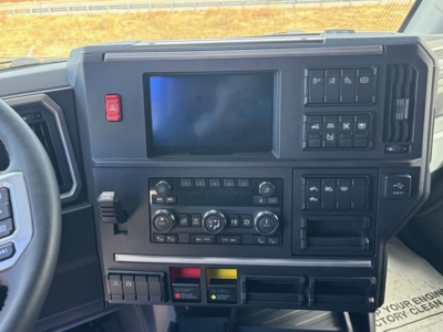 Dashboard view of a 2026 Mack PR64T76H cab area with steering wheel left, large central touchscreen, controls cluster, and various switches.