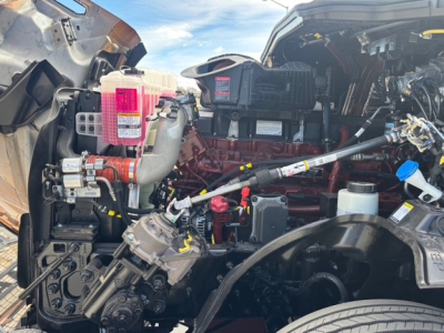 Mack PR64T76H engine bay showing pink coolant reservoir, turbocharger, hoses, wiring harnesses, and engine components.