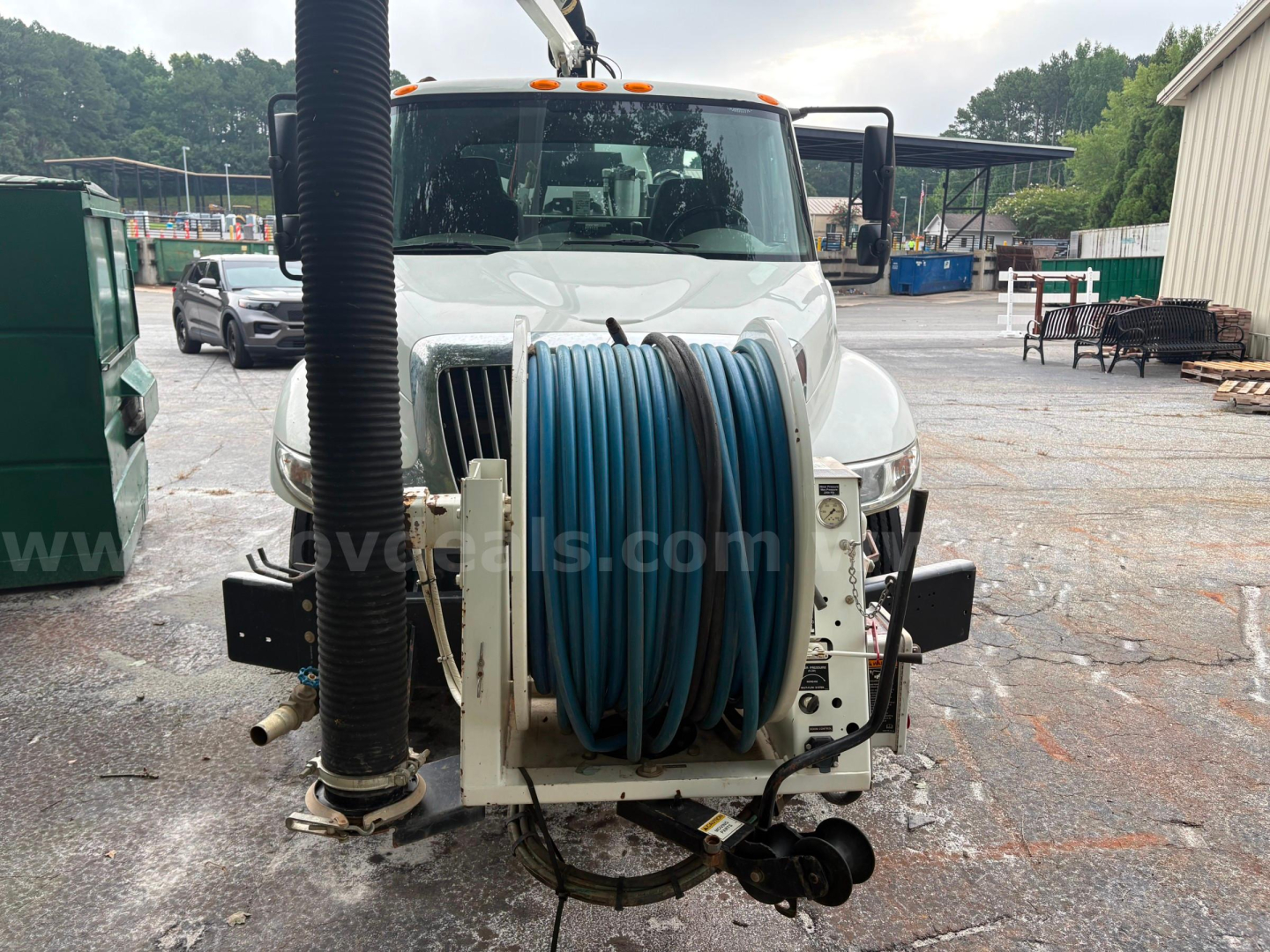 Front view of a 2013 International 4300 vacuum truck with a large blue hose reel mounted on the front bumper area, truck cab in background, utility equipment visible.