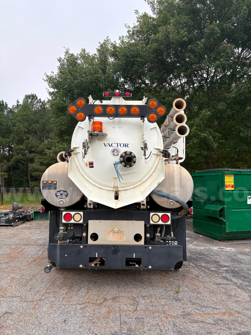 Back view of a vacuum truck tank with two large rear hoses on the right, multiple orange lights, rear bumper, and a circular tank hatch labeled VACTOR.