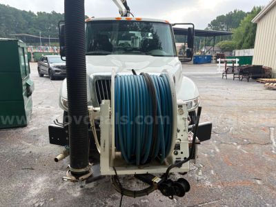 Front view of a 2013 International 4300 vacuum truck with a large blue hose reel mounted on the front bumper area, truck cab in background, utility equipment visible.
