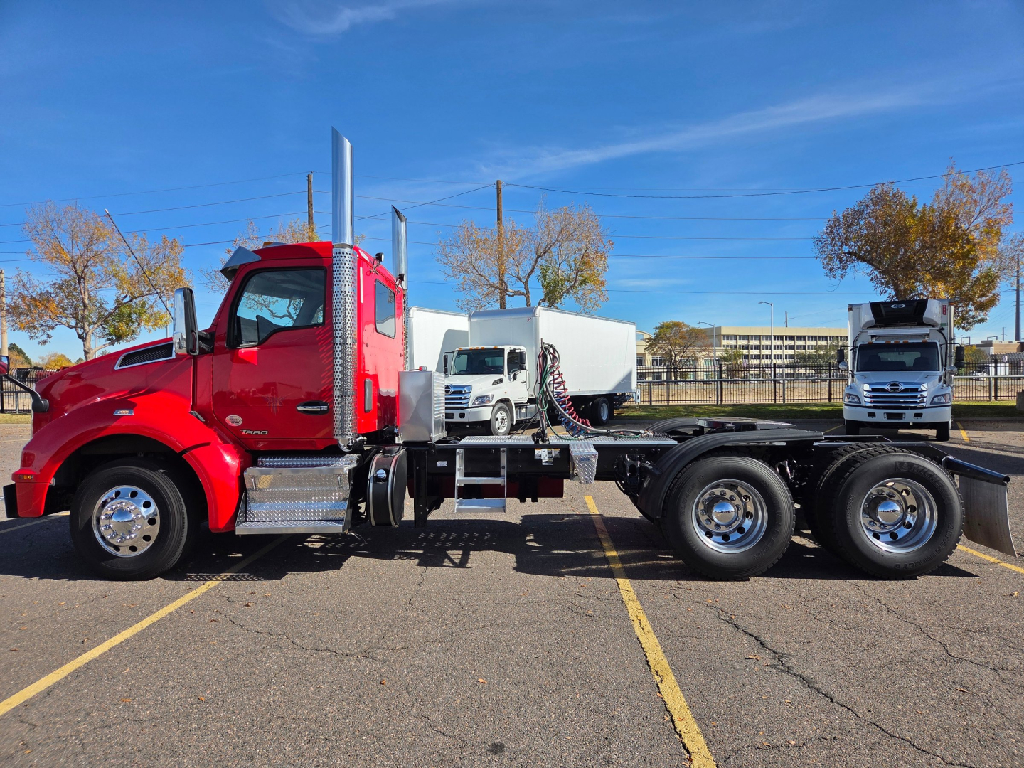 Kenworth T880 conventional daycab tractor in red, side view showing cab, dual rear axles, and chassis in a parking lot.