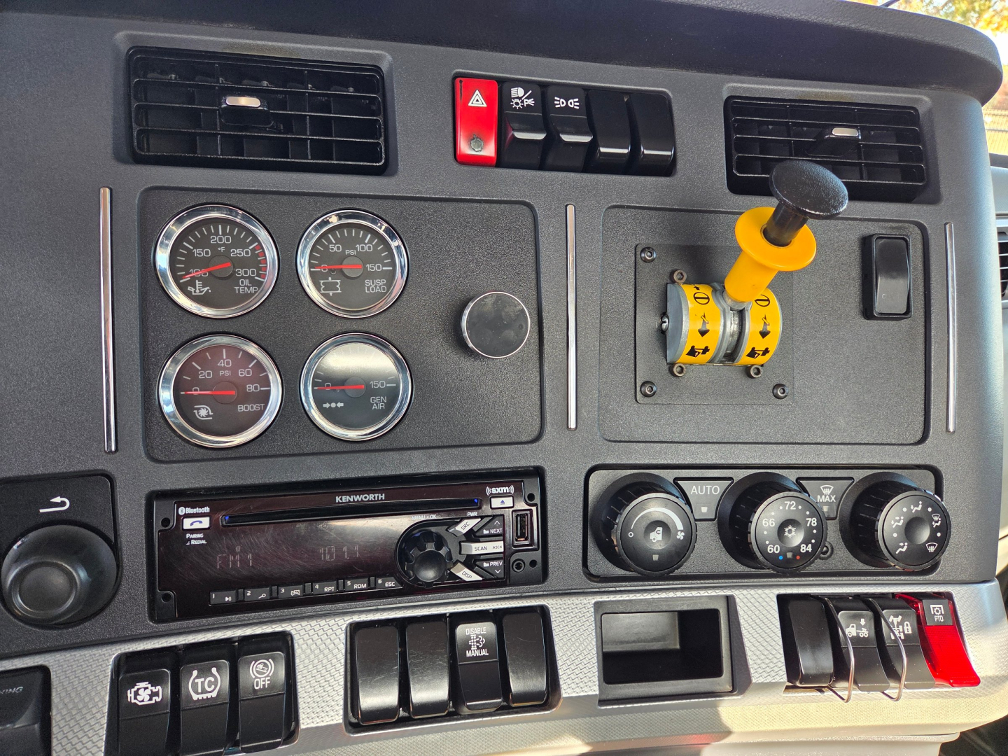 Kenworth T880 dash with four gauges, yellow joystick control, and radio. Visible text includes Kenworth on radio faceplate and various gauge labels.