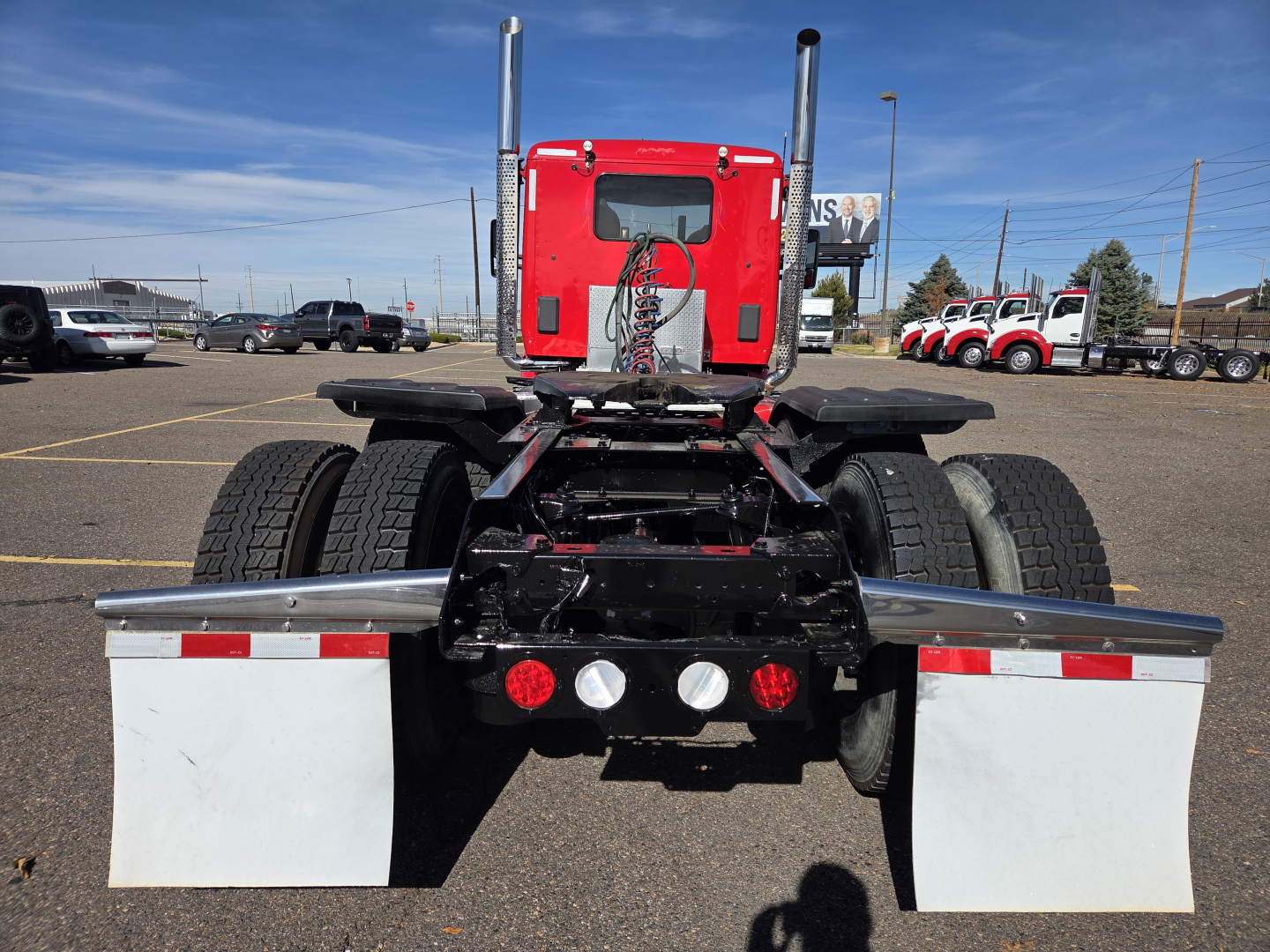 Rear view of a red Kenworth T880 truck chassis showing dual rear axles, mud flaps, and multiple warning lights.