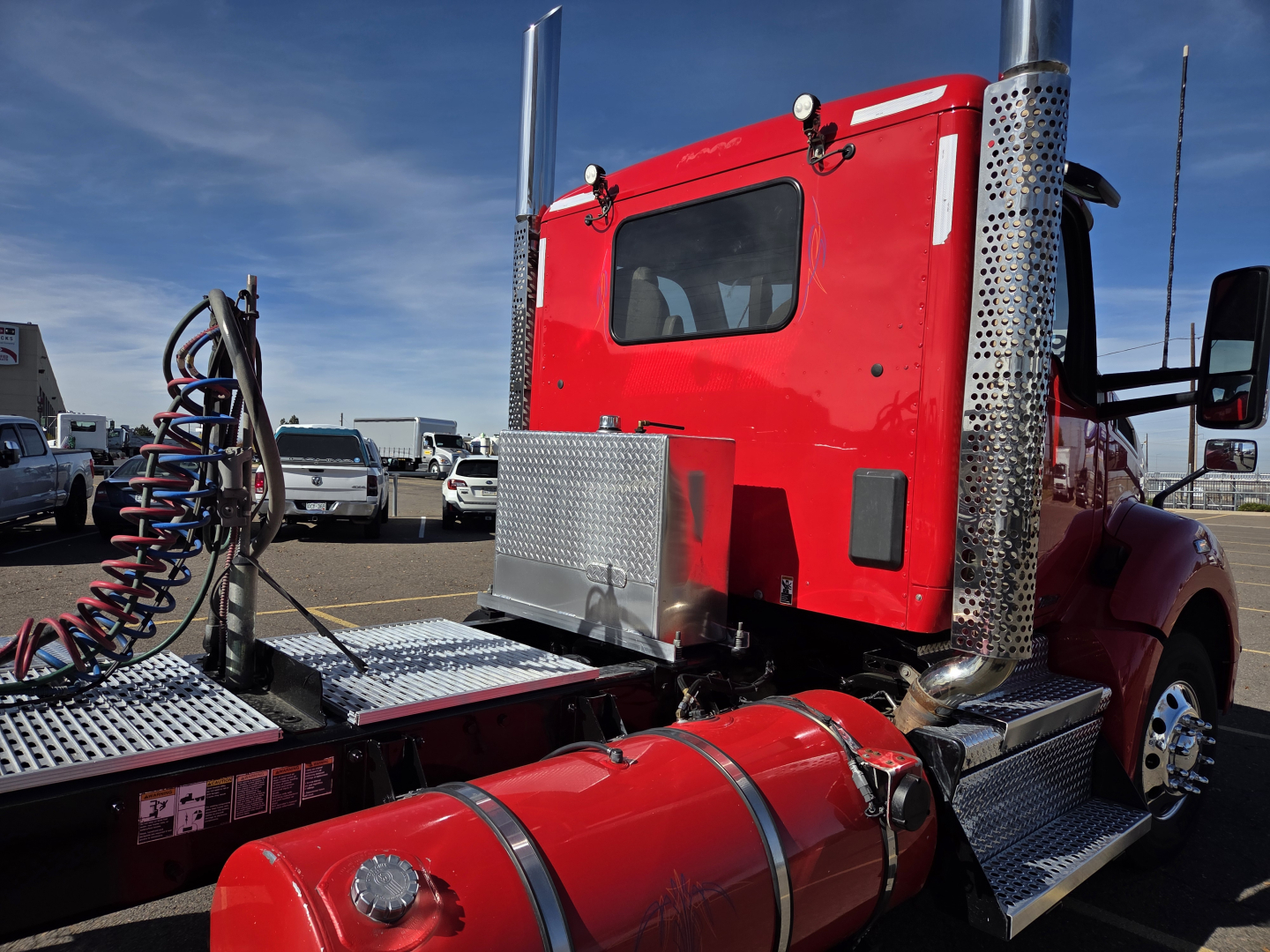 Red Kenworth T880 daytime cab showing side view with chrome exhaust stacks and diamond plate steps and fuel tank.