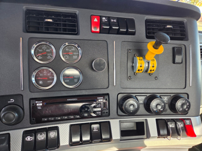 Kenworth T880 dash with four gauges, yellow joystick control, and radio. Visible text includes Kenworth on radio faceplate and various gauge labels.