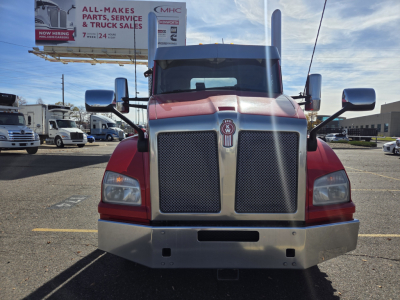 Kenworth T880 front view showing large chrome grille, two rectangular headlights, red cab with black mesh, bumper with fog/air openings, mirrors, and tall exhausts.