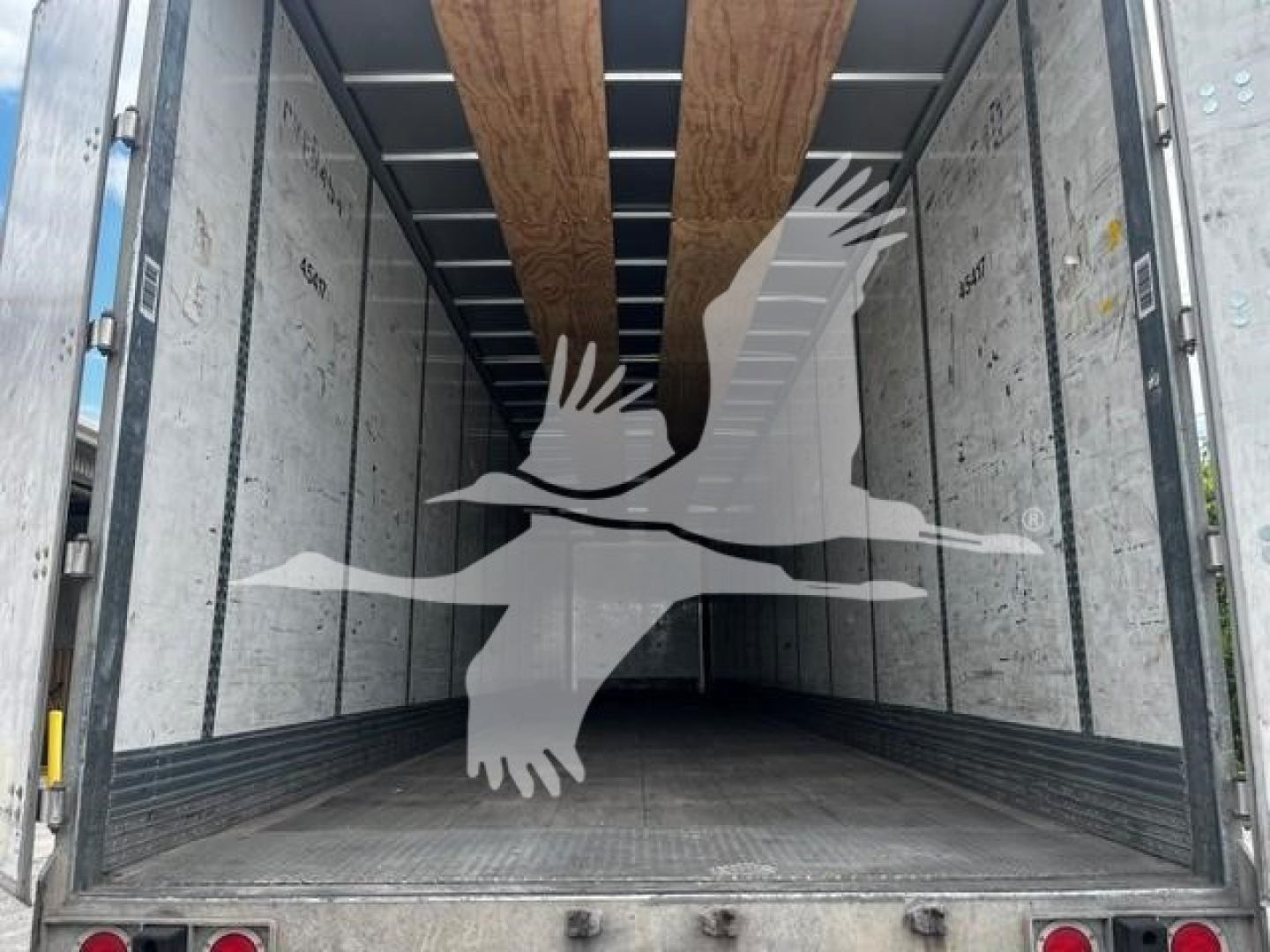 Trailer interior showing empty cargo space with wooden floor runners and metal sidewalls, branding overlay of birds on the image.