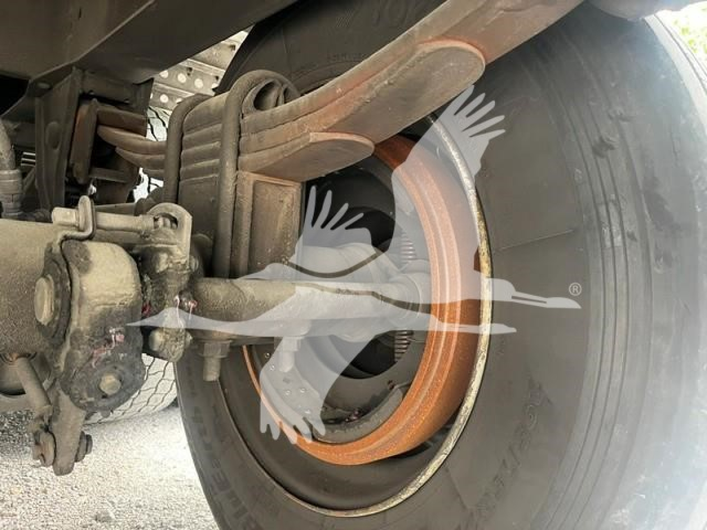 Wheel area of a used trailer showing a large brake drum and suspension components with rust-colored brake lining and leaf springs.
